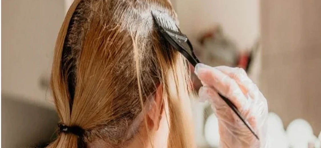 Afbeelding van een vrouw die haar haar kleurt met handschoenen en een verfkwast.